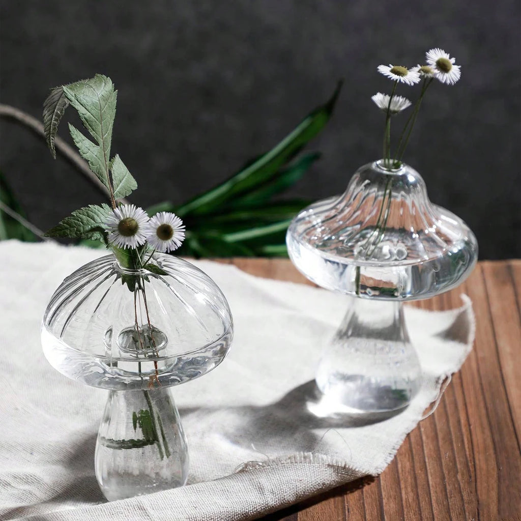Two small glass vases with floral arrangements on a wooden surface.