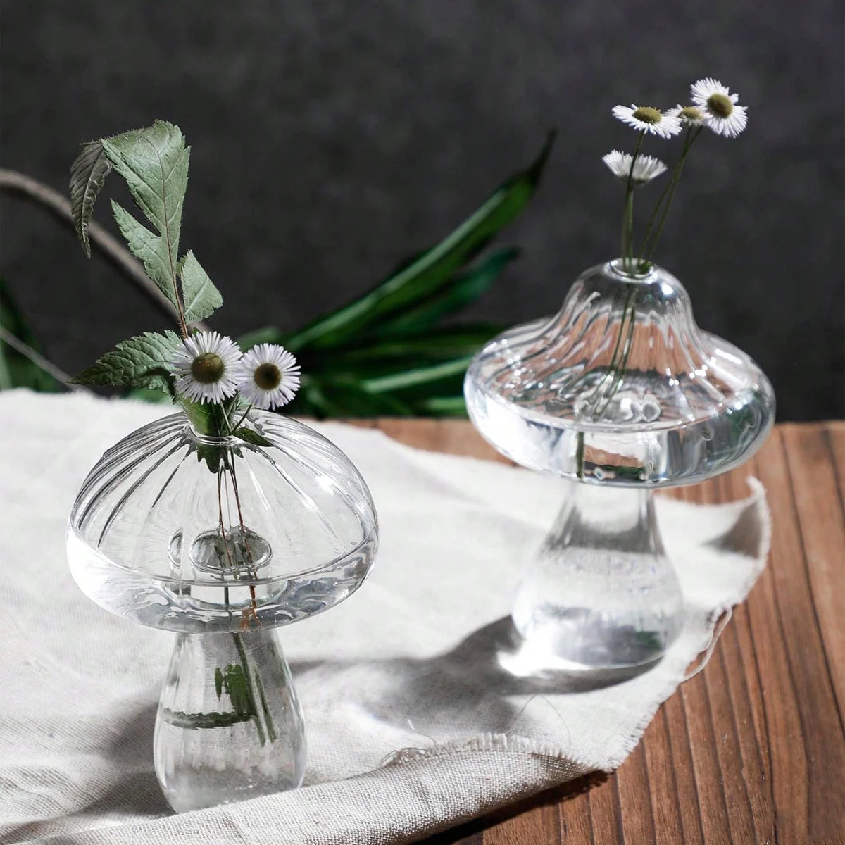 Two small glass vases with floral arrangements on a wooden surface.