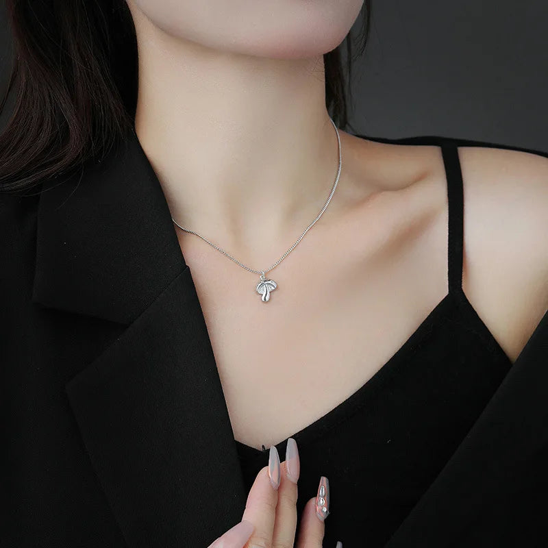 Person wearing a silver necklace with a leaf pendant against a black background