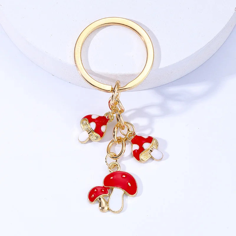 Gold keychain with red mushroom-shaped charms on a white background
