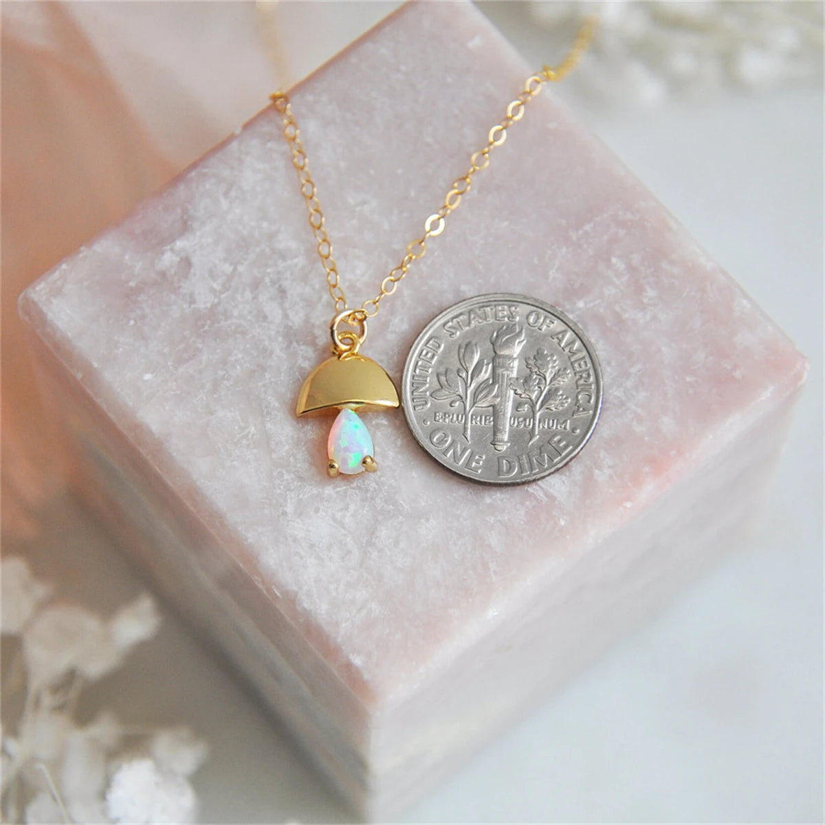 Gold necklace with a pendant on a pink stone surface next to a silver dollar coin.