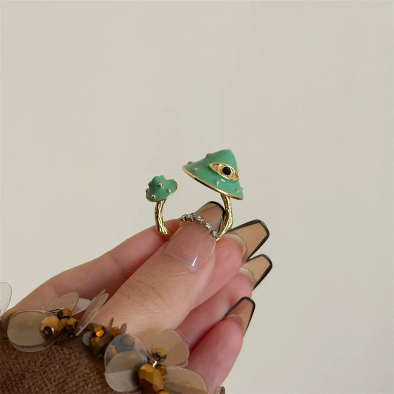 Hand wearing a gold ring with green gemstones on a plain background