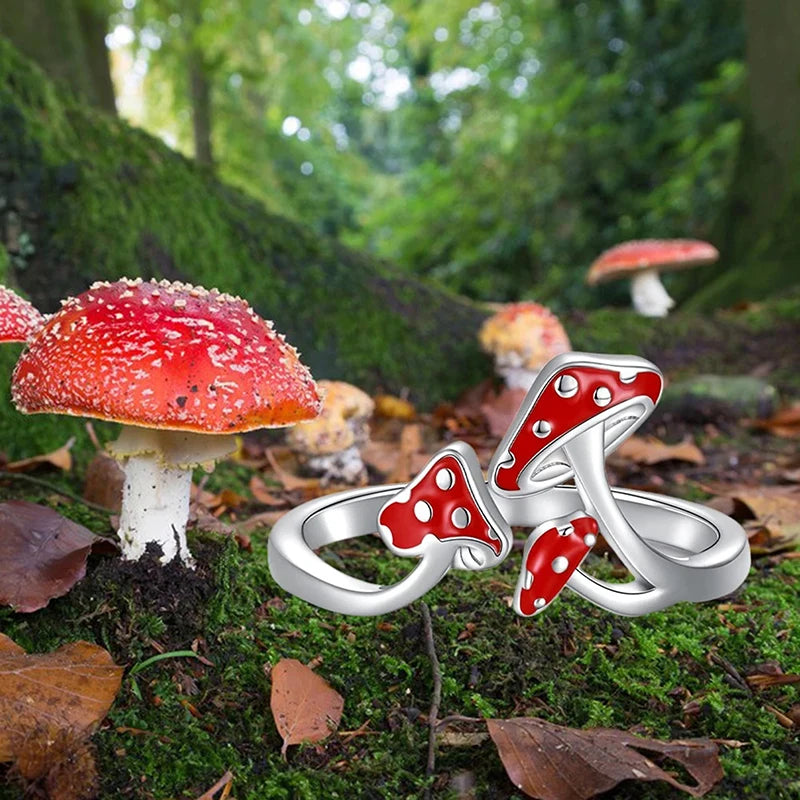 Silver ring with red mushroom design on a forest floor with real mushrooms.
