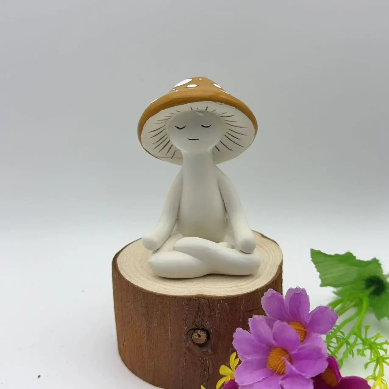 Mushroom-shaped figurine meditating on a wooden block with flowers and leaves in the background
