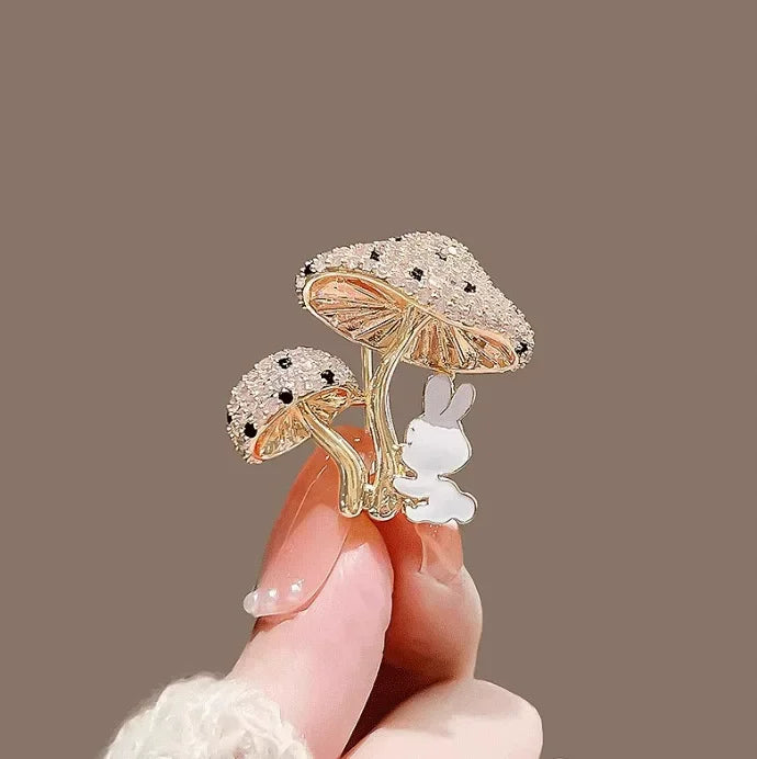 Decorative brooch with mushrooms and a rabbit held by a hand against a brown background