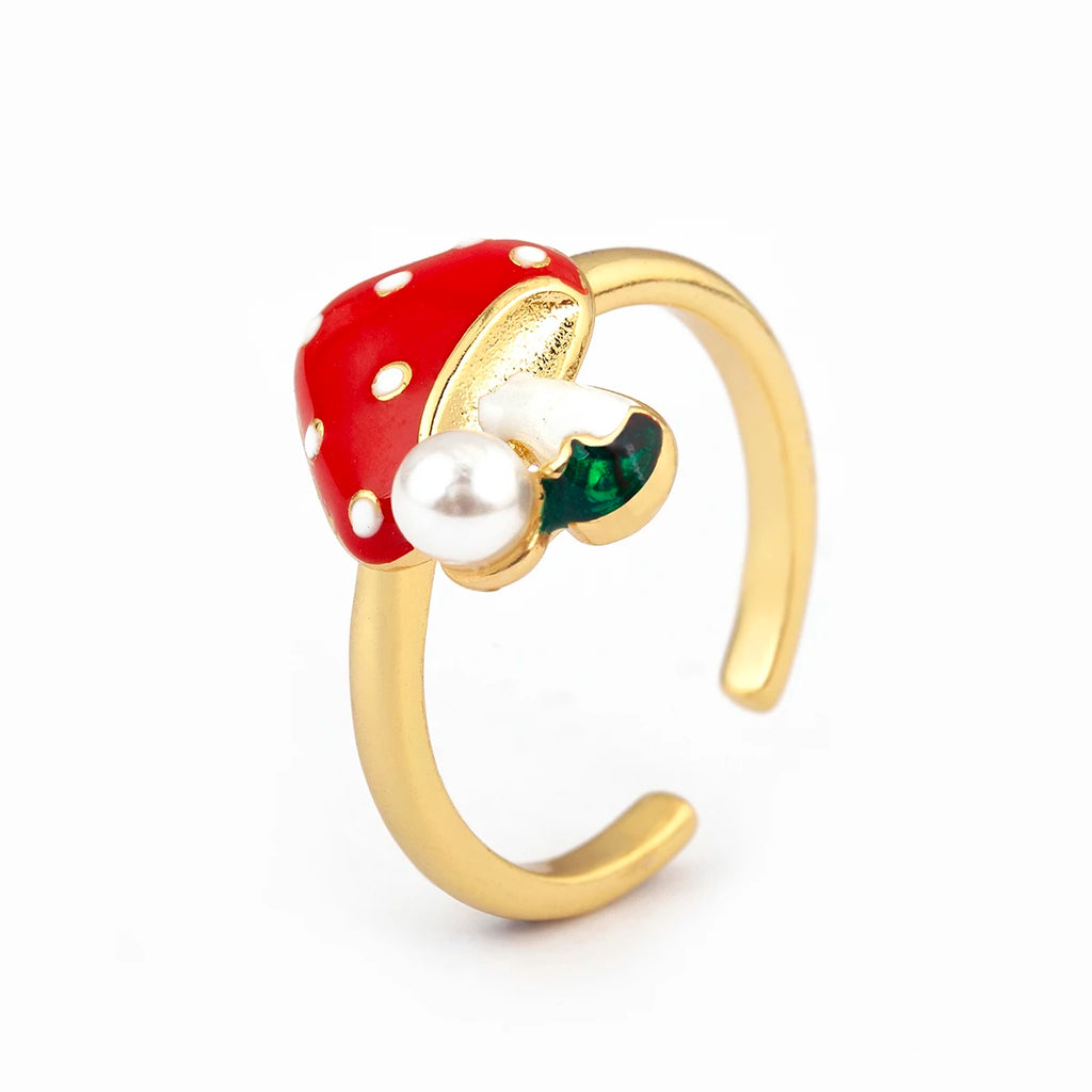 Gold ring with a red mushroom-shaped gemstone, pearl, and green stone on a white background
