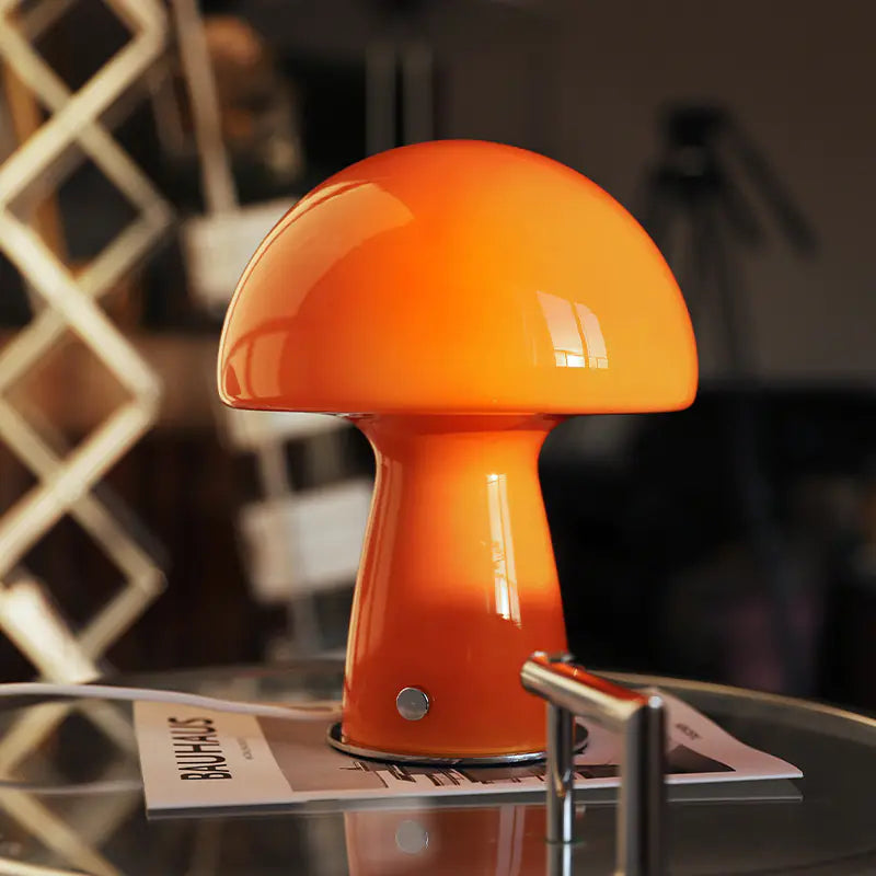 Orange mushroom-shaped lamp on a glass table with a blurred background