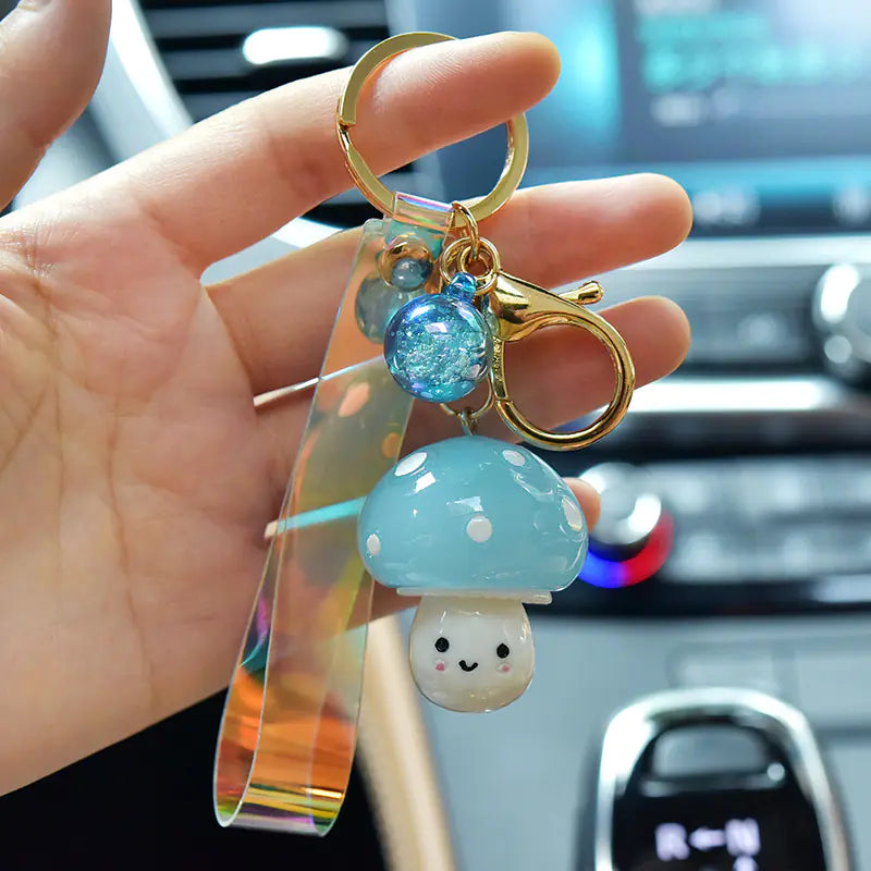 Keychain with mushroom charm held by a hand in front of a car dashboard.
