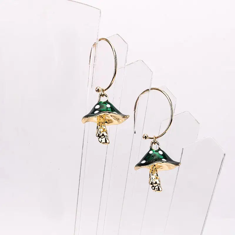 Mushroom-shaped earrings with green caps and gold bases on a clear stand.