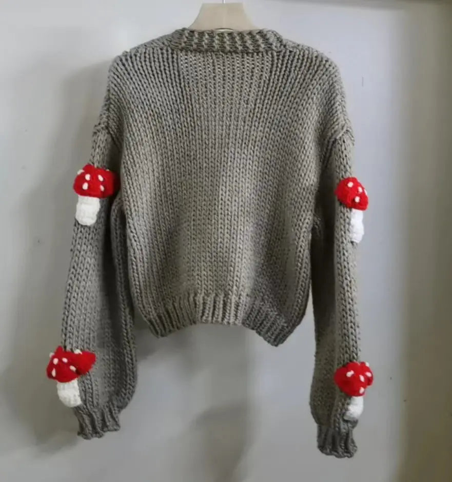 Gray knitted sweater with red mushroom decorations on sleeves and cuffs against a white background