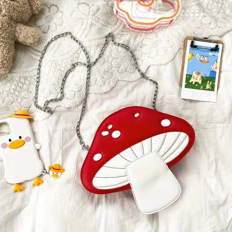 Red and white mushroom-shaped handbag on a textured surface with a phone and plush toy.