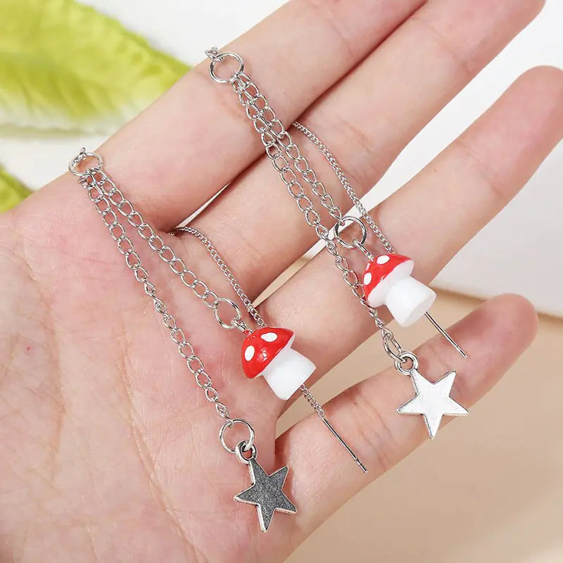Hand holding a silver chain necklace with mushroom and star charms against a blurred background