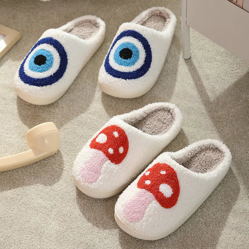 Pair of white slippers with blue and black eye design and red and white mushroom design on a carpeted floor.