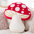 Mushroom-shaped pillow with red cap and white spots on a light-colored couch.