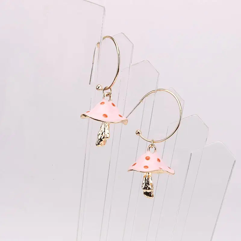Pink mushroom-shaped earrings on a clear stand against a light gray background