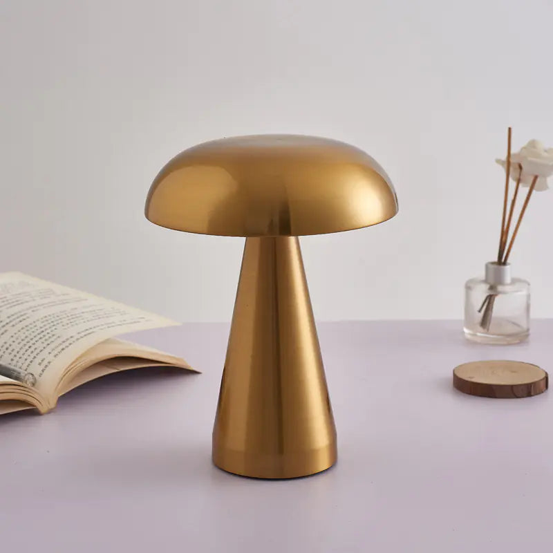 Gold table lamp on a light purple surface with an open book and small vase in the background.
