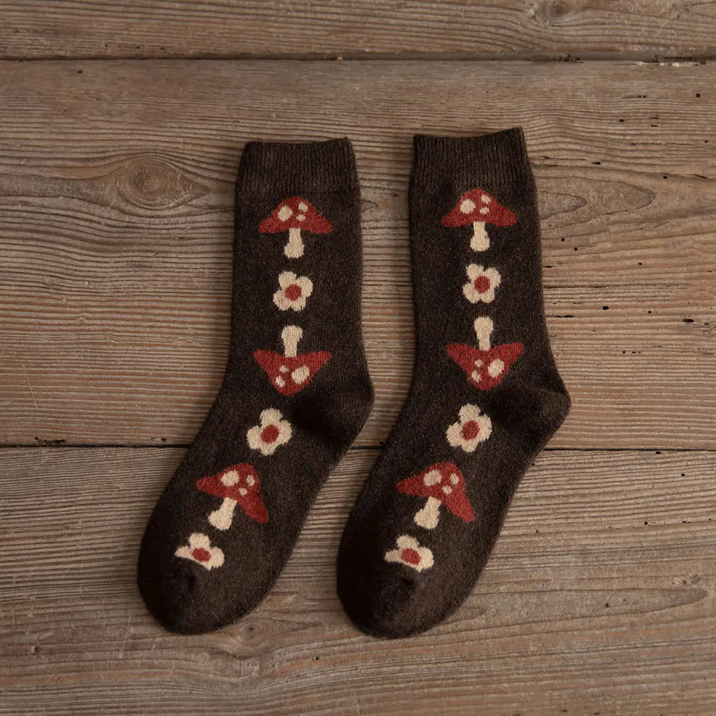 Pair of brown socks with red and white mushroom patterns on a wooden surface